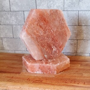 May include: Two pink Himalayan salt blocks, one stacked on top of the other, on a wooden surface. The top block is hexagonal shaped.