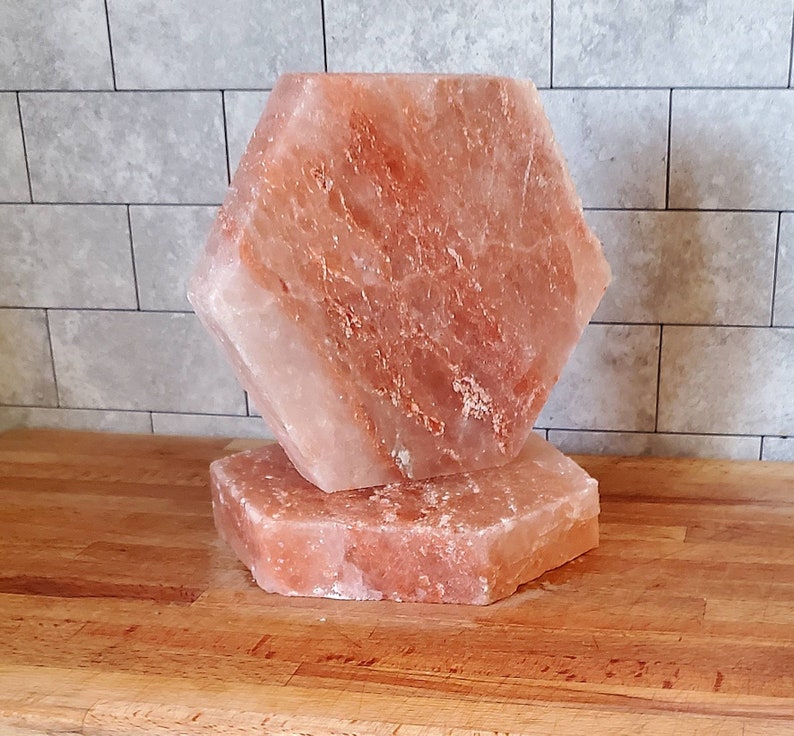 May include: Two pink Himalayan salt blocks, one stacked on top of the other, on a wooden surface. The top block is hexagonal shaped.