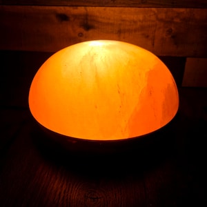 Może przedstawiać: Okrągła, pomarańczowa lampa solna z Himalaj&oacute;w z ciepłym blaskiem. Lampa wykonana jest z naturalnych kryształ&oacute;w soli i jest oświetlona od wewnątrz.