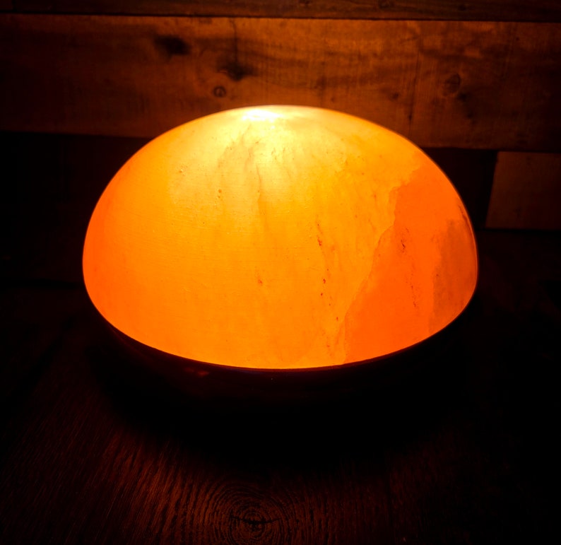 Może przedstawiać: Okrągła, pomarańczowa lampa solna z Himalaj&oacute;w z ciepłym blaskiem. Lampa wykonana jest z naturalnych kryształ&oacute;w soli i jest oświetlona od wewnątrz.