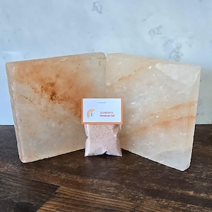 May include: Two large pink Himalayan salt slabs with a small bag of Himalayan salt in the center. The bag has a label that reads "Elementi Himalayan Salt".