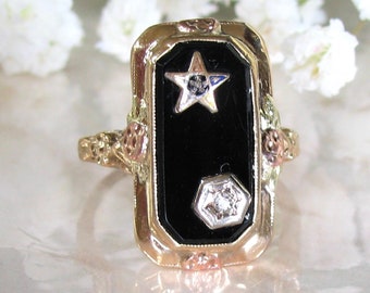 May include: A gold ring with a black onyx stone set in a rectangular frame. The stone is decorated with two small diamonds, one in the shape of a star and the other in a hexagonal shape.