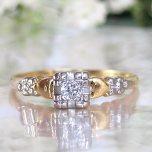 May include: A vintage engagement ring with a single diamond set in a square platinum setting. The band is made of yellow gold and features delicate floral details.