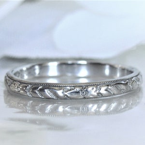 Puede incluir: Una fina banda de boda de plata con un intrincado dise&ntilde;o floral.