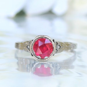 May include: A silver ring with a red ruby gemstone set in a filigree design.