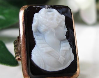 May include: A cameo ring with a white cameo of a woman's profile set in a black onyx stone. The ring is made of gold.