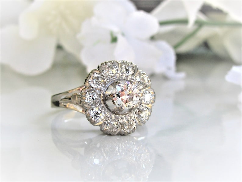 May include: A silver ring with a large, round, clear diamond surrounded by smaller diamonds in a flower-shaped setting.
