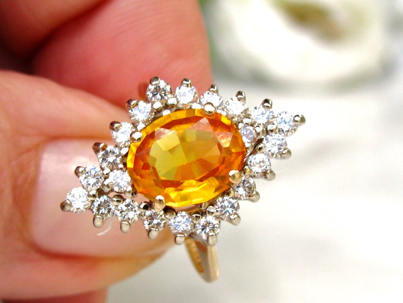 May include: A gold ring with a large oval-shaped orange gemstone surrounded by smaller white gemstones.