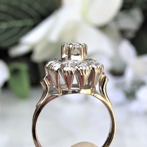 May include: A silver ring with a large, clear center stone surrounded by smaller stones. The ring has a delicate, intricate design.
