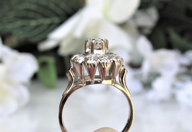 May include: A silver ring with a large, clear center stone surrounded by smaller stones. The ring has a delicate, intricate design.