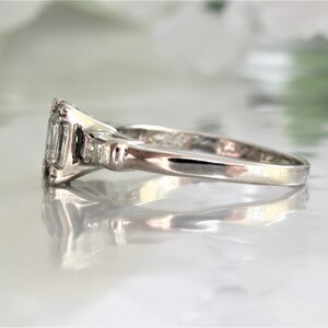 May include: A silver ring with a rectangular-shaped center stone and two smaller stones on either side. The ring is set on a white background.
