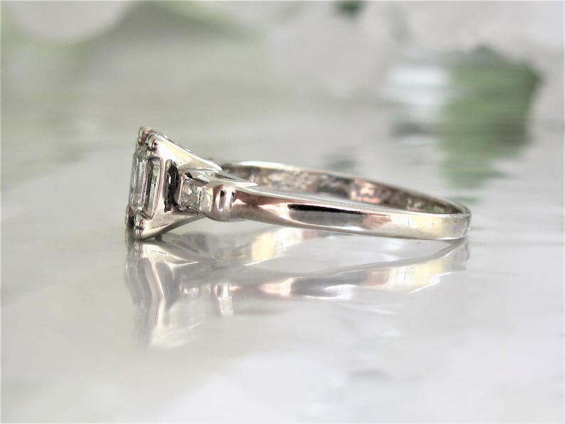 May include: A silver ring with a rectangular-shaped center stone and two smaller stones on either side. The ring is set on a white background.