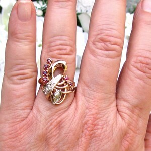 May include: A gold ring with a diamond and ruby stones set in a swirling design.