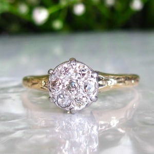 May include: A gold and silver ring with a cluster of small, clear gemstones. The ring has a textured gold band and a silver setting for the gemstones. The ring is a piece of jewelry.