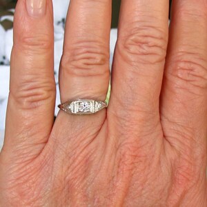 May include: A silver ring with a single round diamond and smaller diamonds on each side. The ring is on a person's finger.