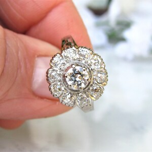 May include: A silver ring with a large round diamond surrounded by smaller diamonds in a flower shape.