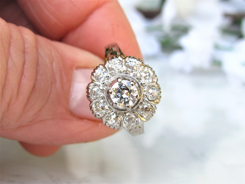 May include: A silver ring with a large round diamond surrounded by smaller diamonds in a flower shape.