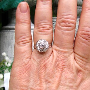 May include: A silver ring with a large round diamond surrounded by smaller diamonds.
