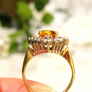 May include: A gold ring with a large, oval-shaped, orange gemstone surrounded by smaller, clear gemstones.
