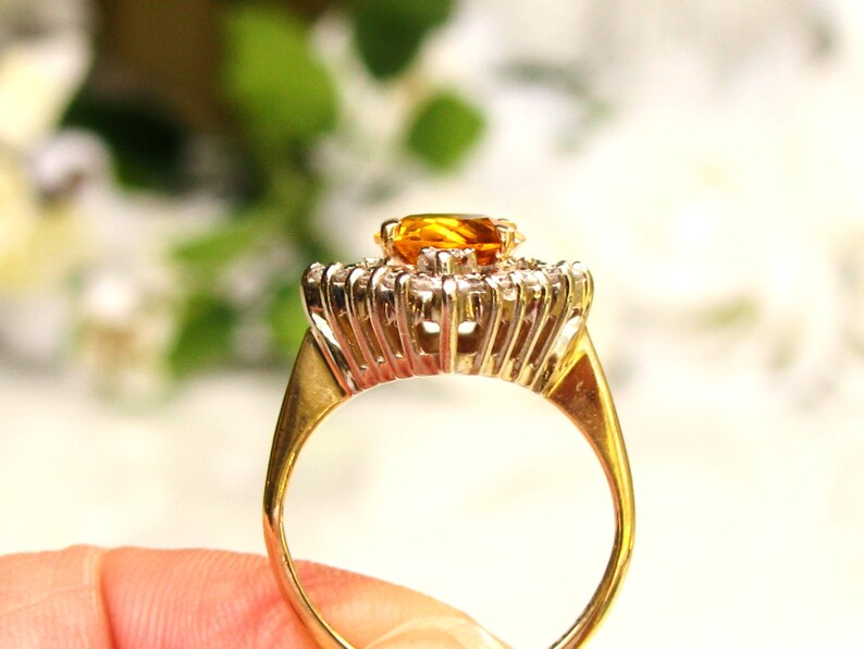 May include: A gold ring with a large, oval-shaped, orange gemstone surrounded by smaller, clear gemstones.