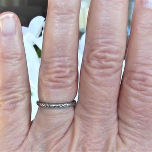 Puede incluir: Un anillo de banda de plata con un dise&ntilde;o texturizado. El anillo se lleva en un dedo.