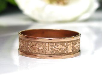 Puede incluir: Un anillo de banda de oro rosa con un diseño grabado detallado. El anillo es una banda simple con un patrón decorativo.