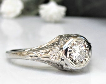 May include: A vintage engagement ring with a delicate filigree design and a single round diamond in a hexagonal setting.