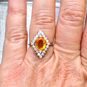 May include: A gold ring with a large oval orange gemstone surrounded by smaller diamonds.