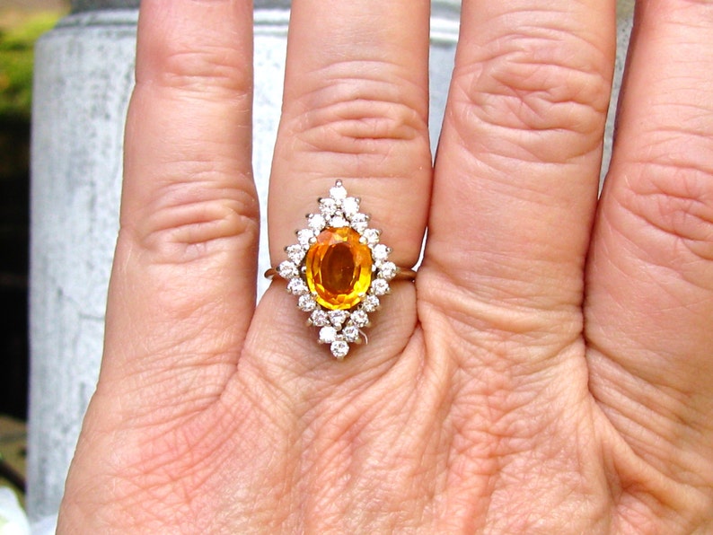 May include: A gold ring with a large oval orange gemstone surrounded by smaller diamonds.