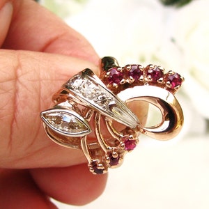 May include: A gold ring with a marquise-shaped diamond and ruby accents. The ring features a delicate, intricate design with a bow-like shape.