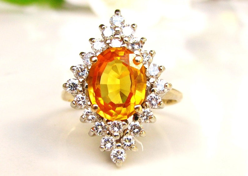 May include: A gold ring with a large oval-shaped orange gemstone surrounded by smaller clear gemstones.