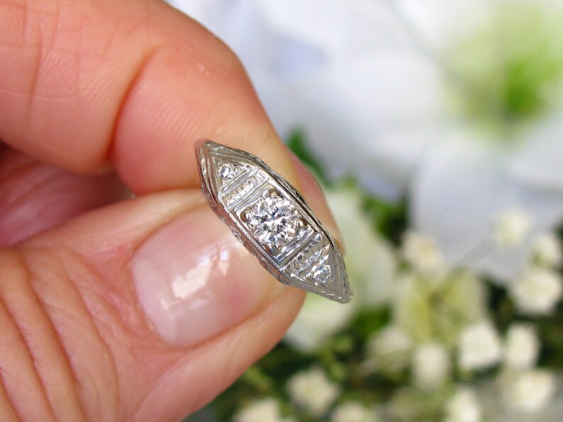 May include: A silver engagement ring with a central diamond and smaller diamonds set in a delicate, intricate design.