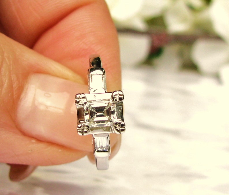 May include: A silver engagement ring with a square-shaped diamond and two smaller diamonds on the band.