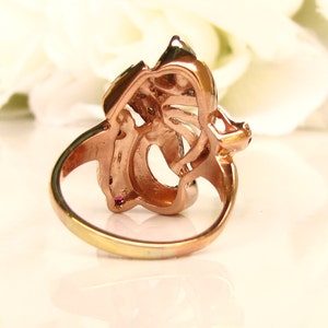 May include: A rose gold ring with a floral design. The ring is set with clear and pink stones.