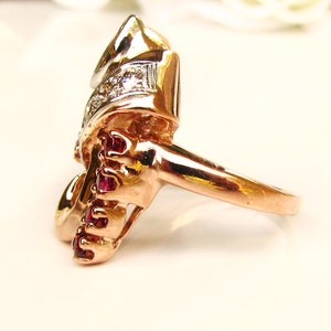 May include: A gold ring with a unique design featuring a cluster of red rubies and a smaller cluster of white diamonds.