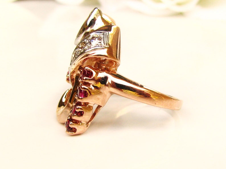 May include: A gold ring with a unique design featuring a cluster of red rubies and a smaller cluster of white diamonds.