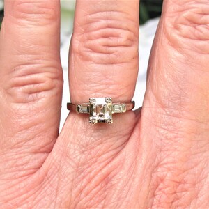 May include: A silver ring with a square-shaped center diamond and two smaller baguette diamonds on either side.