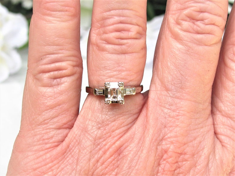 May include: A silver ring with a square-shaped center diamond and two smaller baguette diamonds on either side.