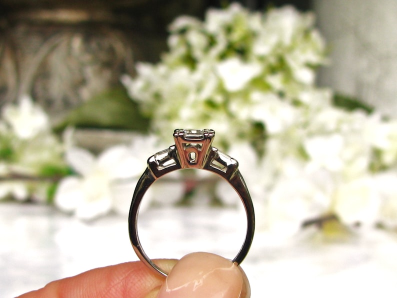 May include: A silver engagement ring with a square-cut center stone and two smaller baguette-cut stones on either side.
