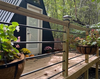 May include: A black triangular cabin with a wooden deck and black metal railing. The cabin has a white door and a window. There are potted plants on the deck.
