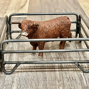Peut inclure: Une figurine de vache Highland brune debout dans un enclos à bétail en métal. L'enclos est en acier soudé et a une forme carrée.