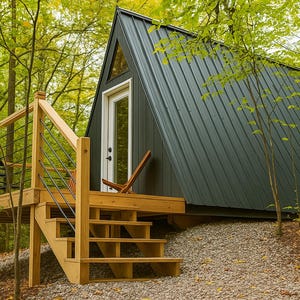Puede incluir: Cabaña en forma de A con techo de metal gris oscuro y puerta blanca, ubicada en un bosque. La cabaña tiene una terraza y escaleras de madera con una barandilla sencilla. Una silla de madera está en la terraza. Los árboles circundantes tienen hojas verdes y amarillas.
