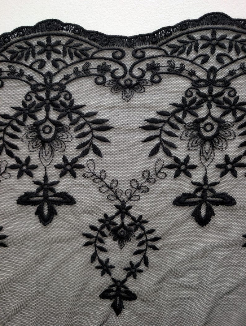 Puede incluir: Una tela de encaje negro con un intrincado patr&oacute;n floral bordado y un borde festoneado. El dise&ntilde;o consta de motivos bot&aacute;nicos sim&eacute;tricos, que incluyen hojas, peque&ntilde;as flores y enredaderas, cosidos sobre una base de malla transparente.