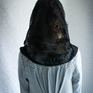 May include: A woman wearing a black lace veil over a light blue blouse with lace trim. The blouse has a button closure in the back.