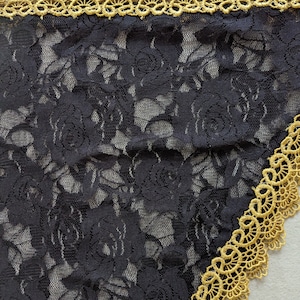 May include: Close-up of black lace fabric with a rose pattern. The edge is trimmed with gold-colored lace, creating a decorative border. The intricate design and contrasting colors highlight the delicate texture of the lace.