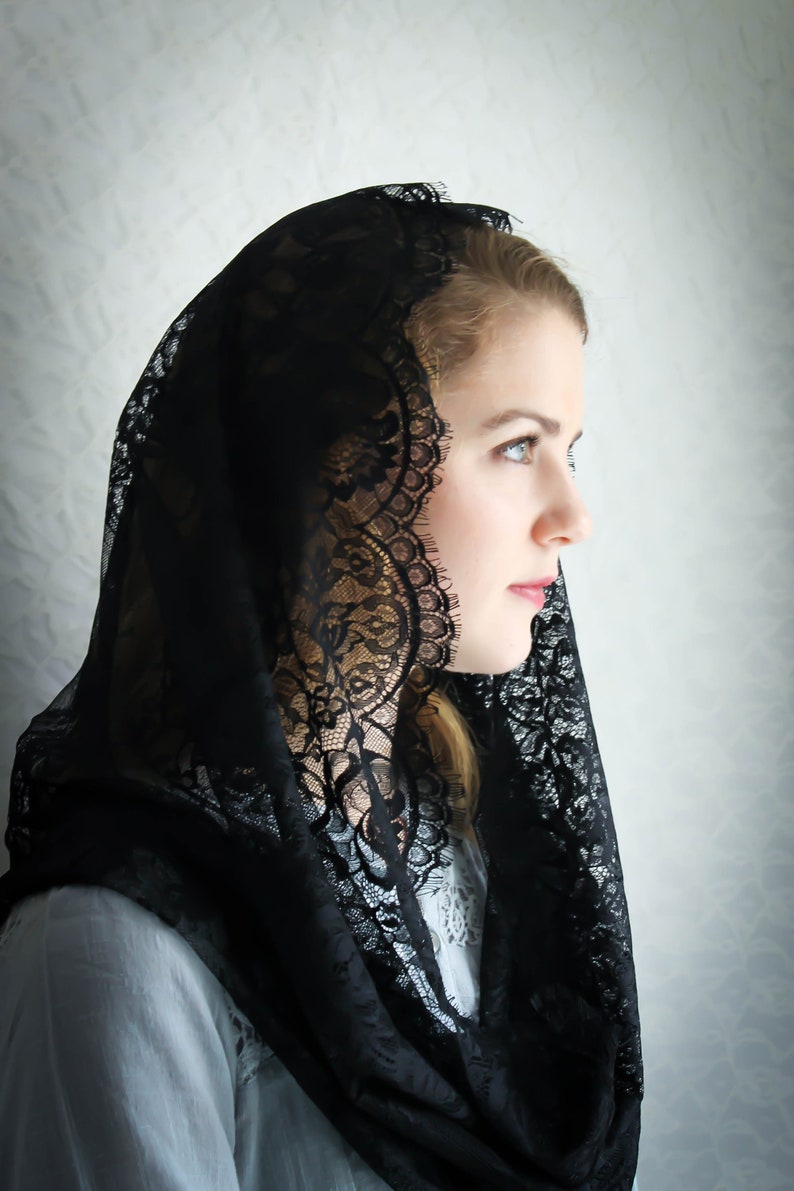 May include: A woman wearing a black lace mantilla, a traditional head covering.