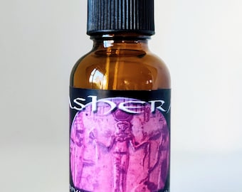 May include: An amber glass dropper bottle with a black cap. The label features a circular pink graphic of an ancient Egyptian figure and the text: ASHTER, DIVINE ELIXIR 1 OZ, USE 3 TO 20 DROPS, ATHERA STAR GODDESS. The bottle has a black rubber dropper top.