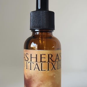 May include: An amber glass dropper bottle with a black cap. The label features the text ASHERA'S VITALIXIR in black lettering, with additional text reading CRYSTALLINE COPPER NANO-PARTICLES and USE 5-15 DROPS 1-2 TIMES A DAY on a tan background.