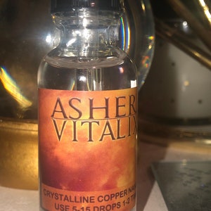 May include: A clear glass bottle with a black dropper top. The label reads "ASHER VITALIX" in large white letters over a gradient orange background. Below, it says "CRYSTALLINE COPPER NAN" and "USE 5-15 DROPS 1-2 TIMES".