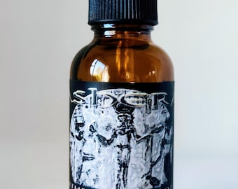 May include: An amber glass dropper bottle with a black cap. The black label features a white illustration of figures and the text: SIDRA, MOTHERS ELIXIR 1 OZ, USE 3 TO 20 DROPS, NHERA STAR GODDESS. The bottle contains a liquid and has a glass dropper top.
